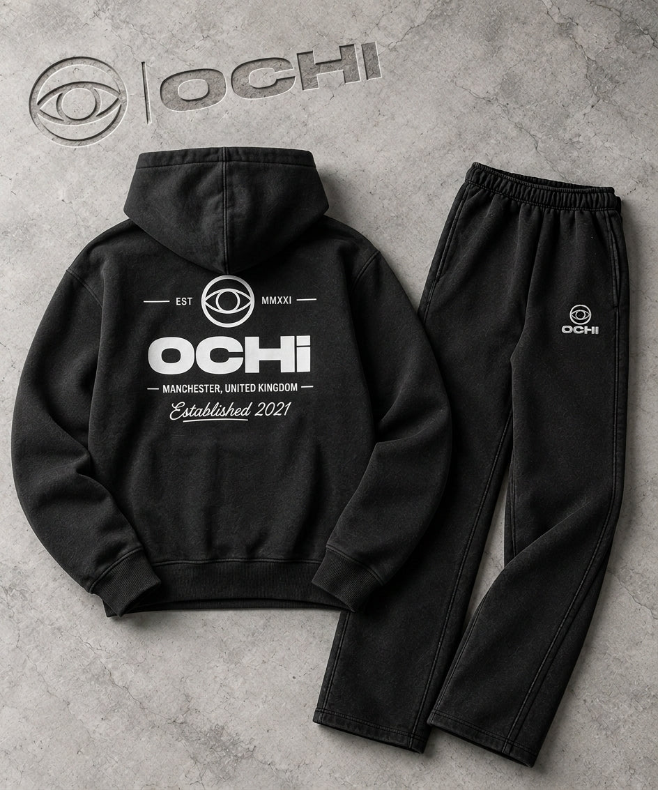 Black OCHI World UK hoodie and joggers with Manchester and Established 2021 branding, photographed on a textured concrete background